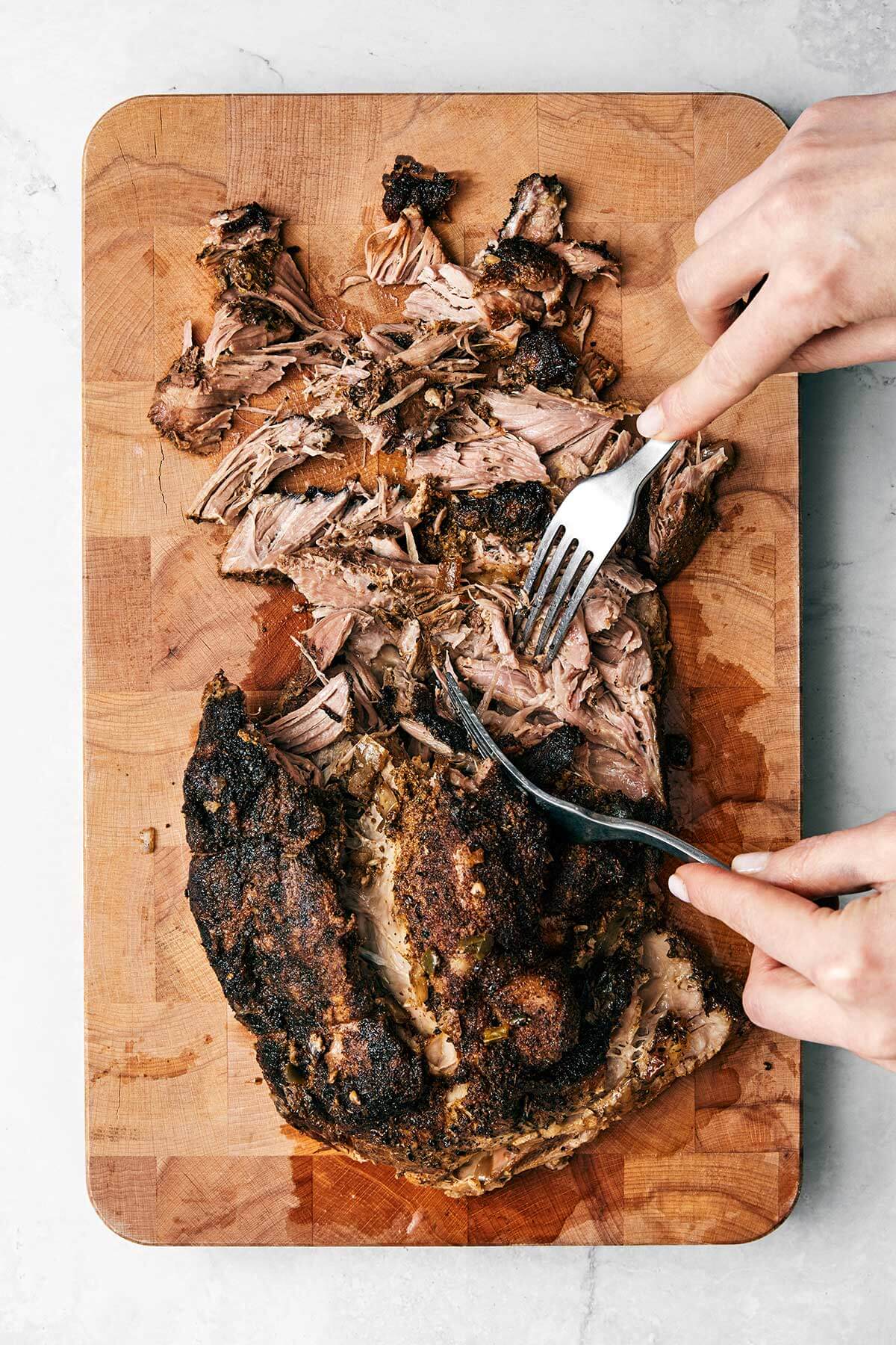 The best Mexican carnitas recipe that's juicy, full of flavor, fall-apart tender, and super easy to make in a slower cooker! Shredding carnitas on a wooden board.