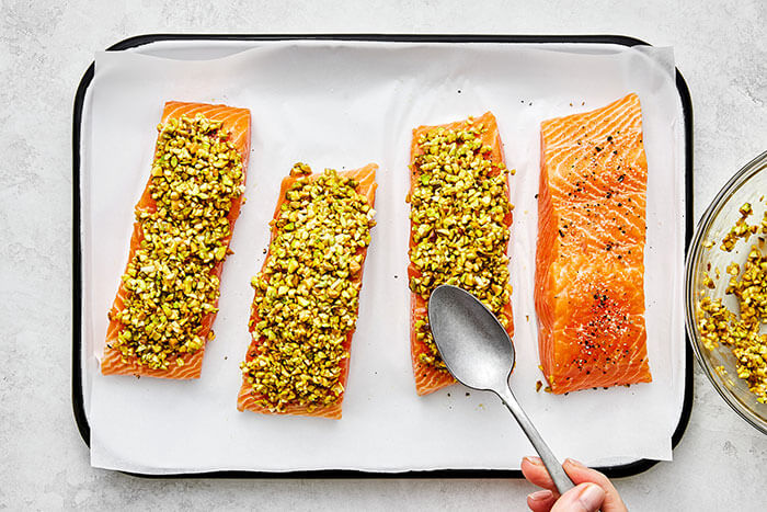 Spooning pistachio topping onto salmon