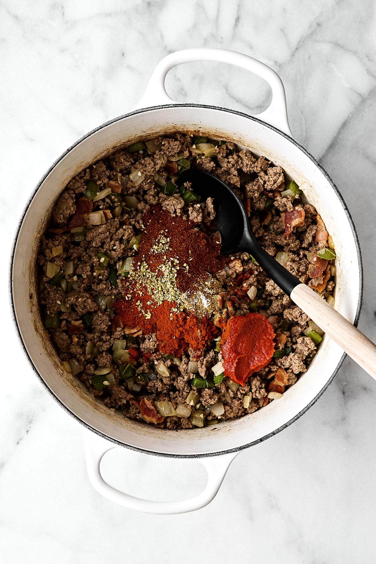 Adding seasonings to a pot of beef chili.