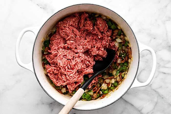 Adding ground beef to a pot of chili.