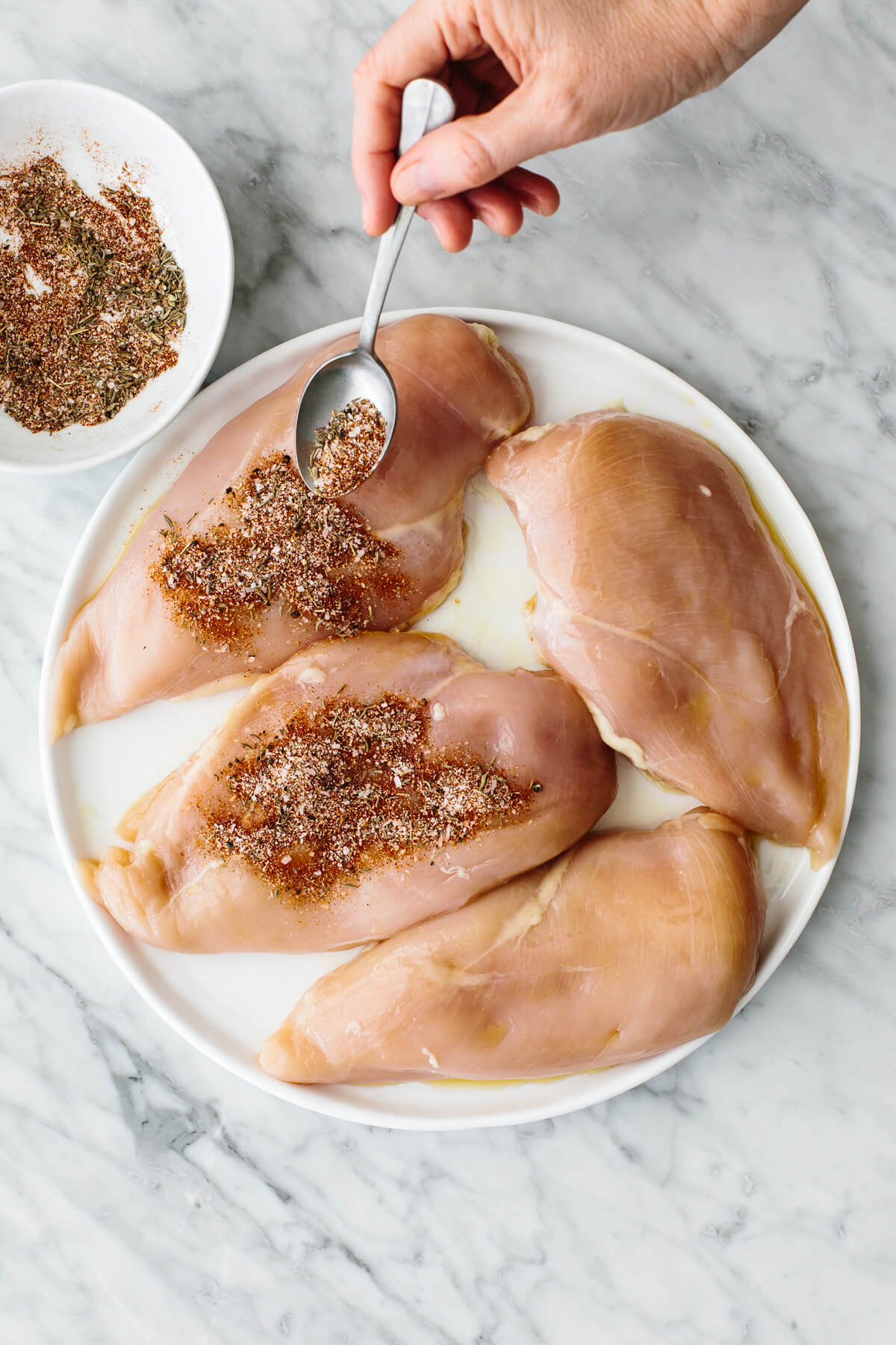 Seasoning the chicken breasts.