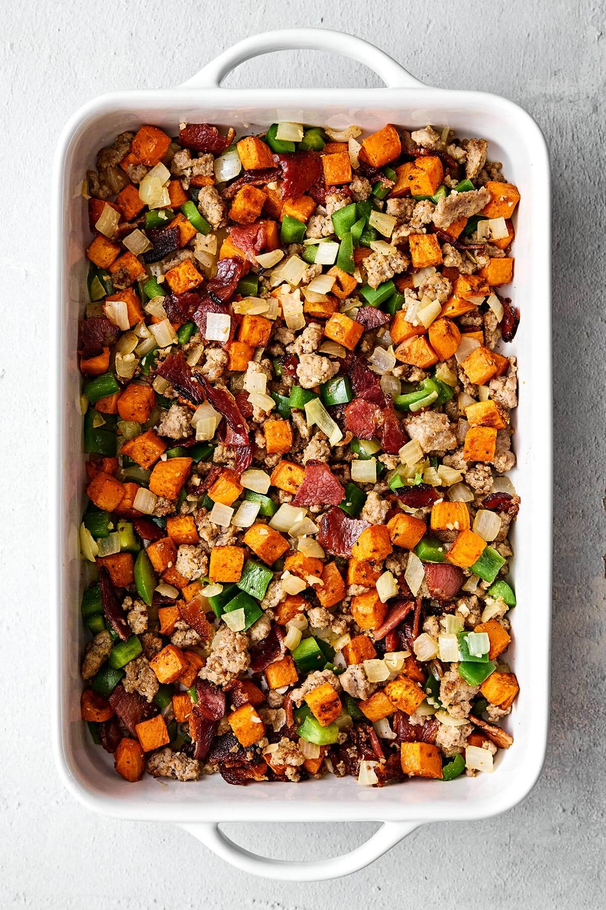 This is the best breakfast casserole loaded with bacon, sausage, sweet potatoes, and plenty of veggies. Plus, it's always a crowd favorite! Prepping a breakfast casserole in a baking dish.