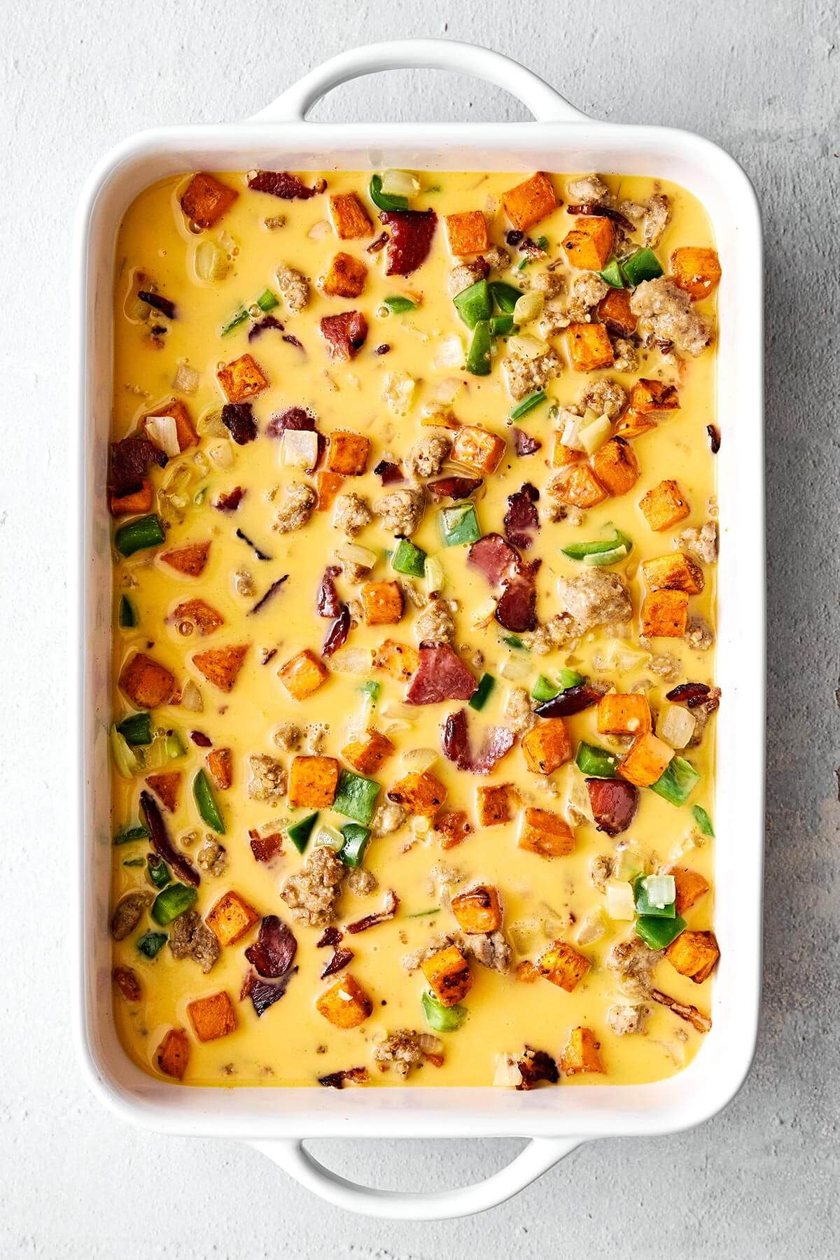 This is the best breakfast casserole loaded with bacon, sausage, sweet potatoes, and plenty of veggies. Plus, it's always a crowd favorite! Eggs, meats, and veggies in a baking dish.