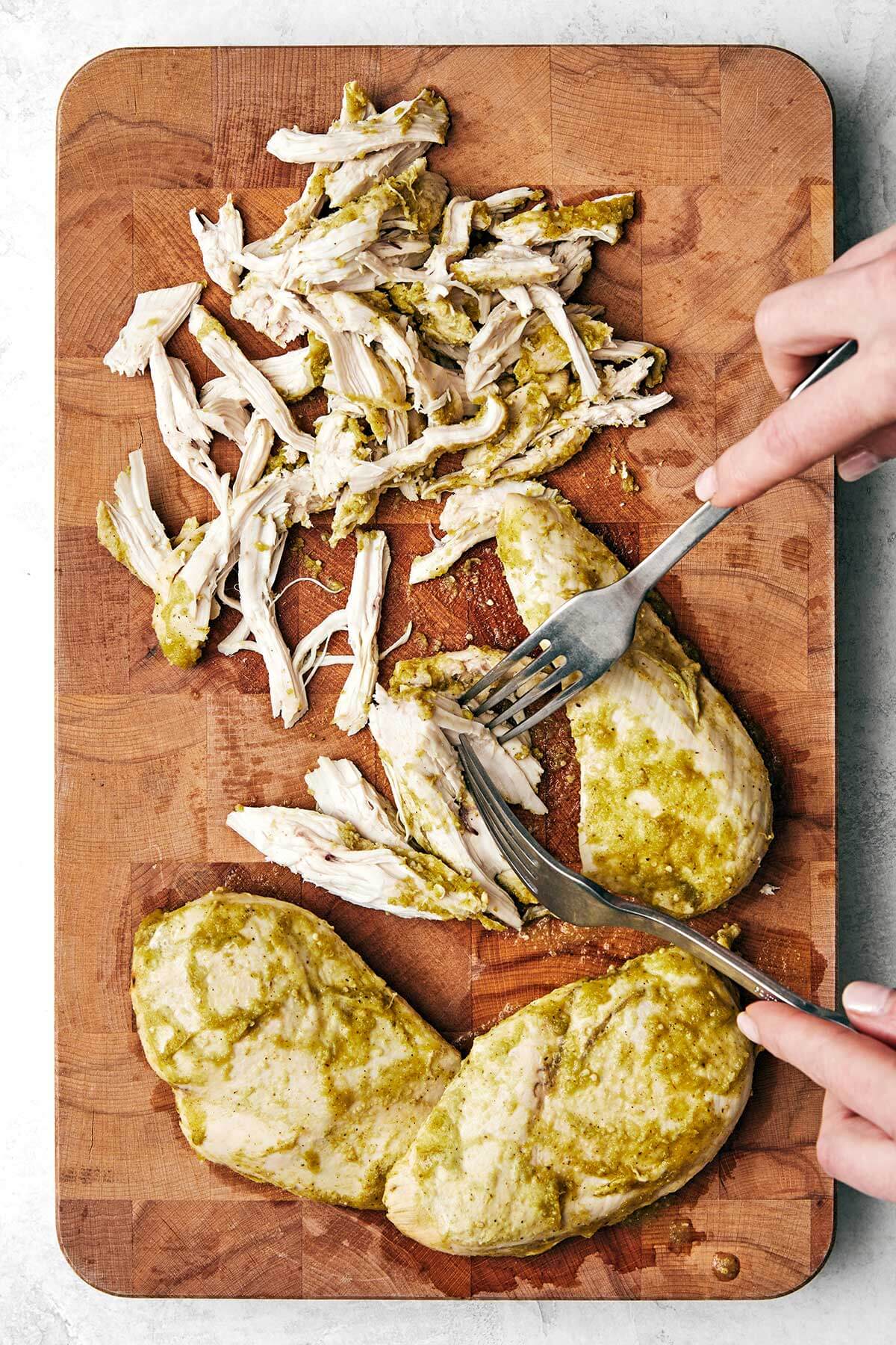 Shredding salsa verde chicken on a wooden board.