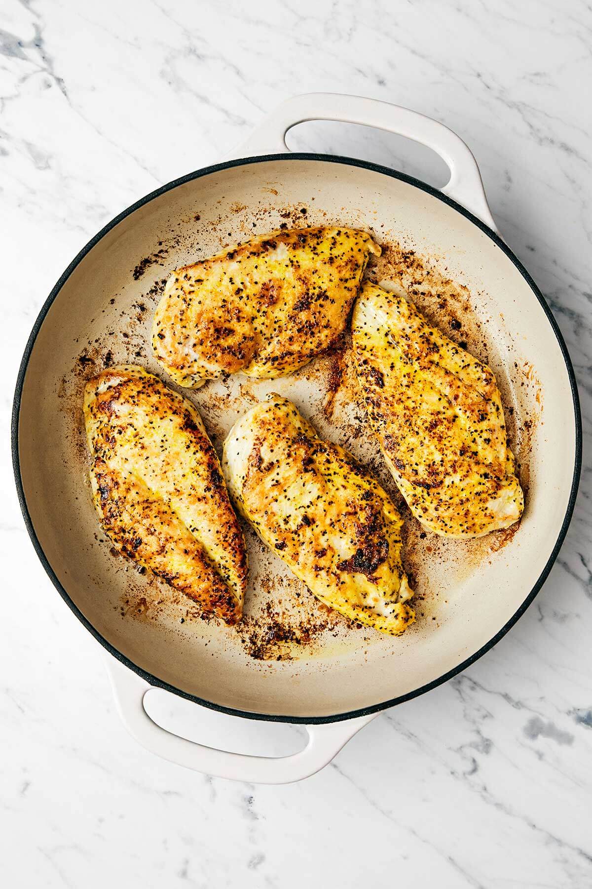 This lemon pepper chicken dinner is perfect for busy weeknights. It's bright and tangy with a golden crust and topped with a garlic butter sauce. Seared chicken breasts in a pan.