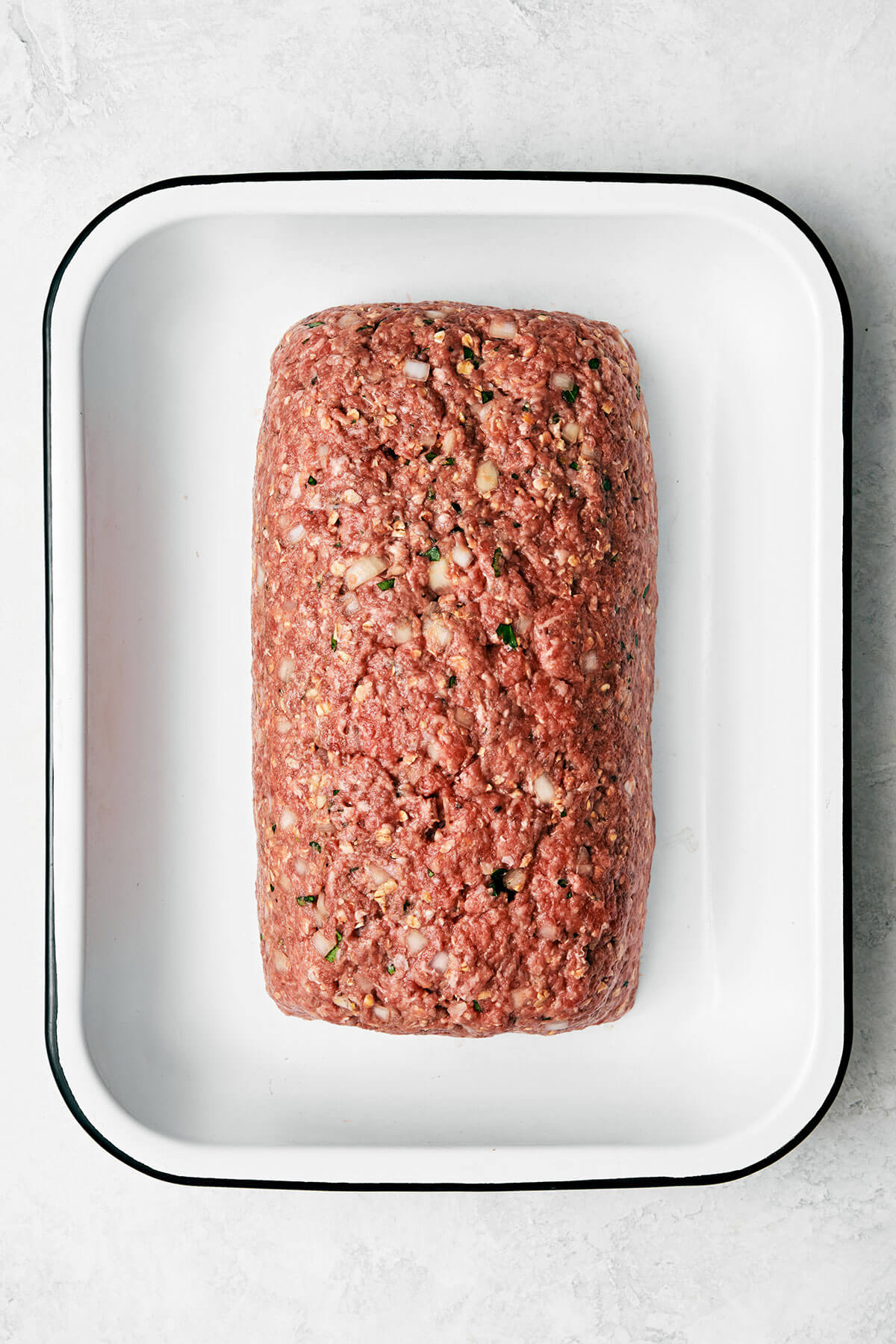 Here's my secret to the best classic meatloaf recipe! It's tender and moist, layered with flavor, and brushed with a tasty meatloaf sauce! Raw meatloaf in a pan.