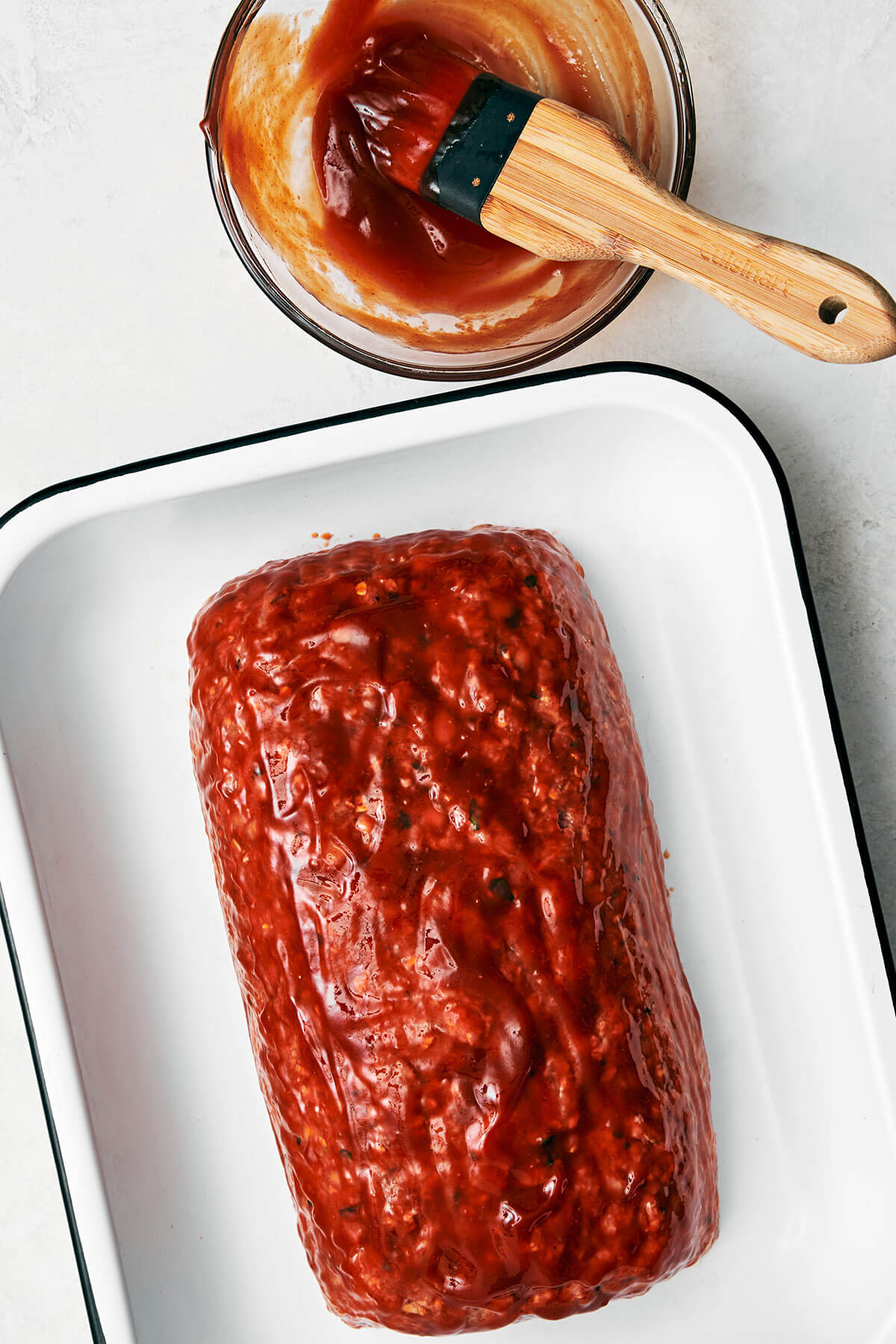 Here's my secret to the best classic meatloaf recipe! It's tender and moist, layered with flavor, and brushed with a tasty meatloaf sauce! Brushing sauce on meatloaf.