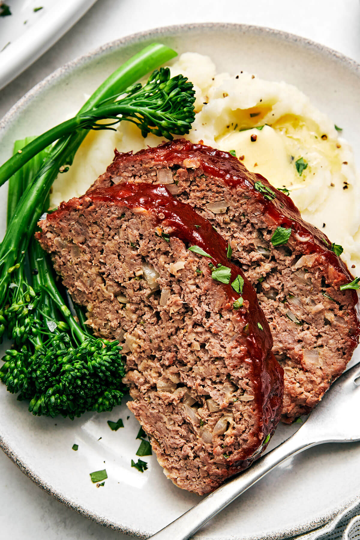 Here's my secret to the best classic meatloaf recipe! It's tender and moist, layered with flavor, and brushed with a tasty meatloaf sauce! Sliced meatloaf with broccolini and mashed potatoes.