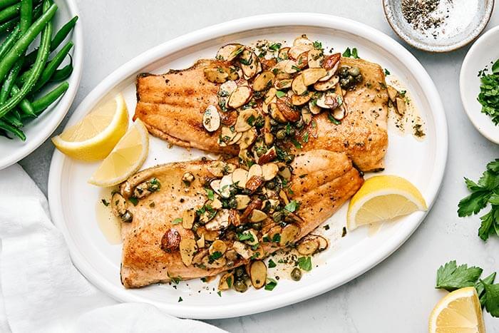 A white plate of rainbow trout almondine.