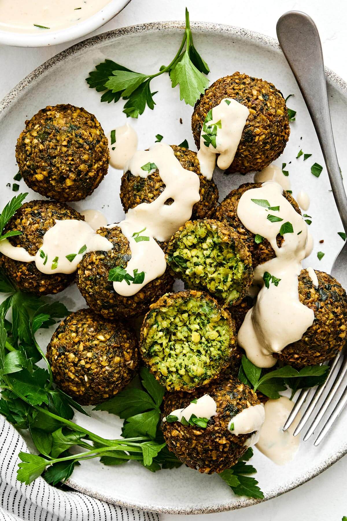 Falafel are delicious balls of chickpea and herb goodness in Middle Eastern cooking. They're naturally vegan and vegetarian, and great in wraps, pitas, sandwiches and salads. You can make fried falafel and baked falafel - I've got instructions for both! Falafels with tahini sauce and a fork.