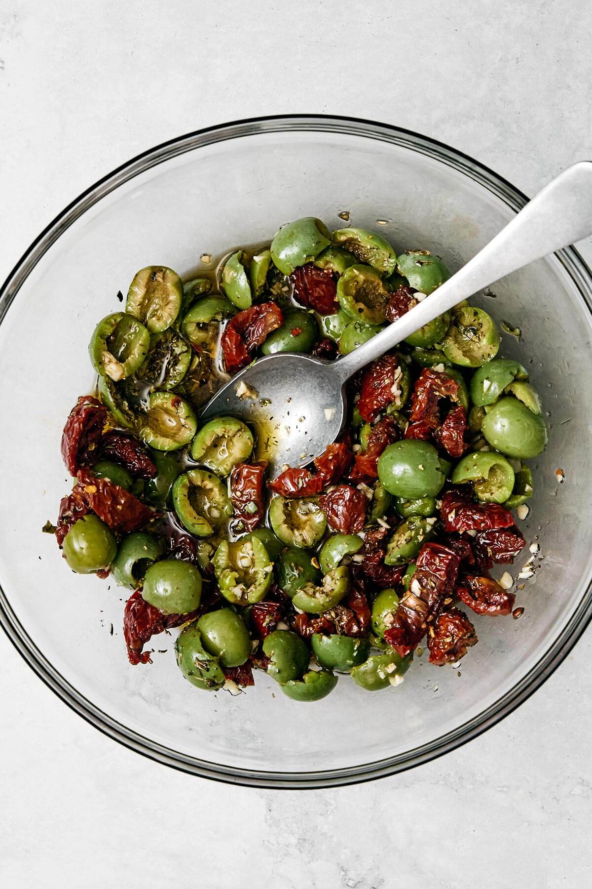 This Mediterranean baked feta with an herb-infused olive and sundried tomato topping is officially my signature appetizer for dinner parties. Stirring olives and sun-dried tomatoes.