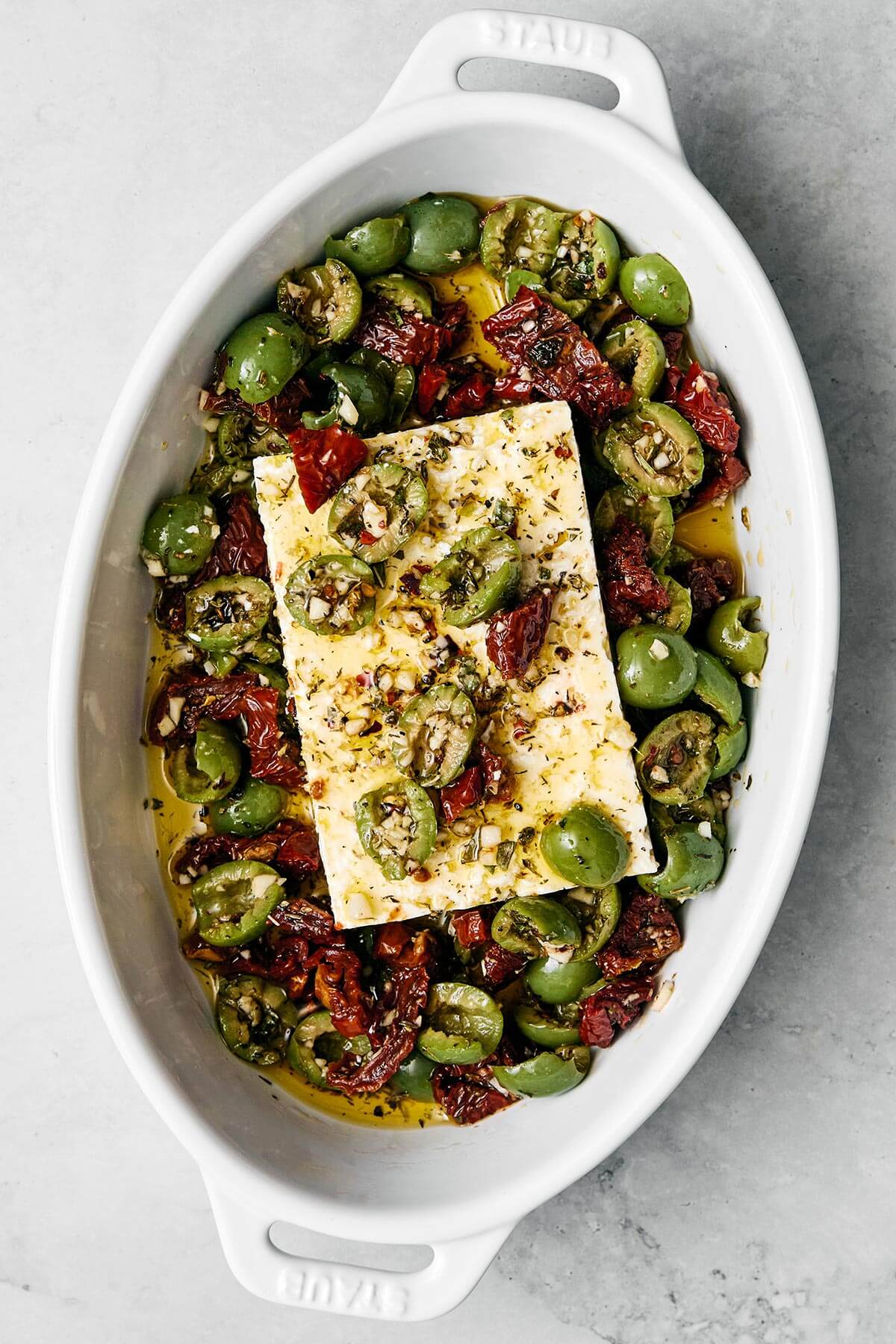 This Mediterranean baked feta with an herb-infused olive and sundried tomato topping is officially my signature appetizer for dinner parties. A baking dish with feta cheese and olives.