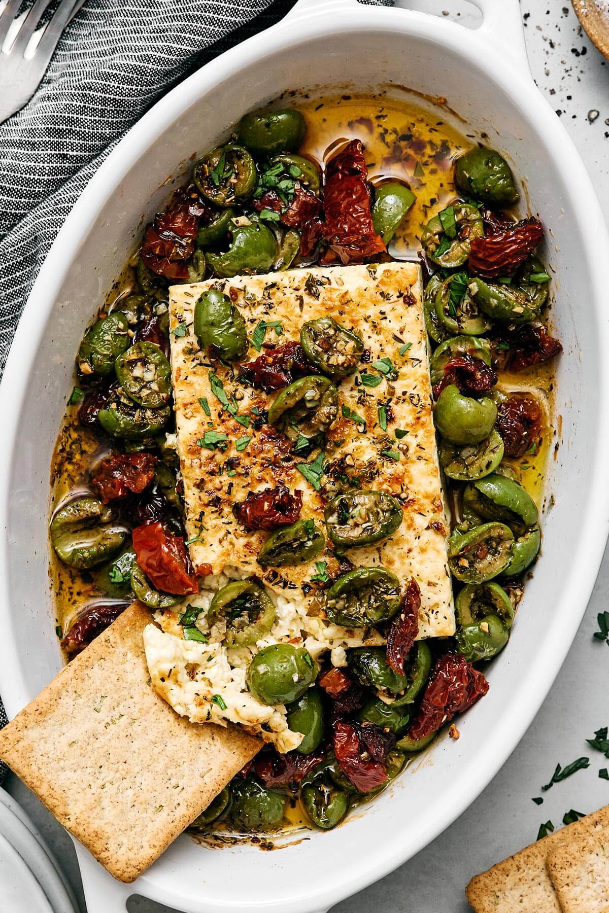 This Mediterranean baked feta with an herb-infused olive and sundried tomato topping is officially my signature appetizer for dinner parties. Mediterranean baked feta with a cracker.