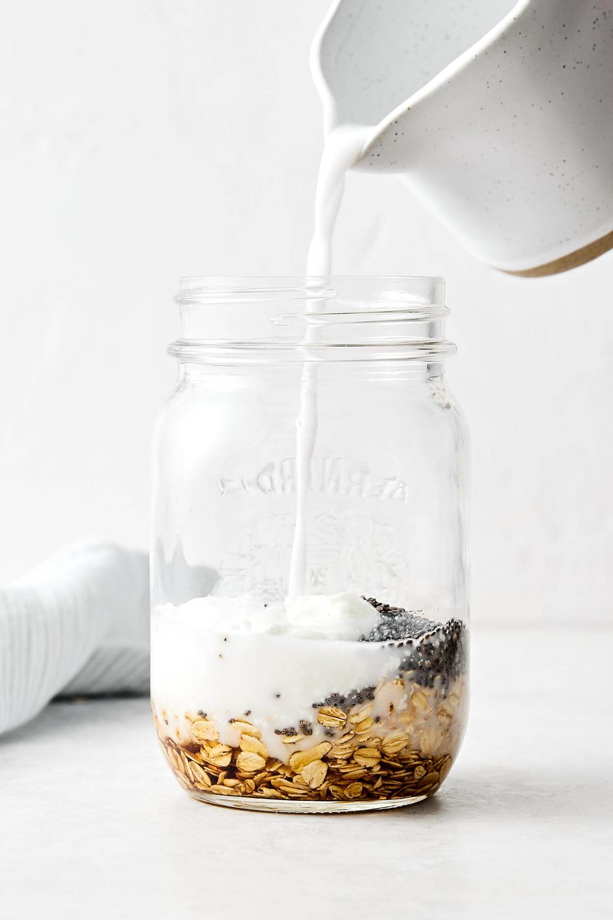 Learn how to make the perfect batch of overnight oats! This version is made with rolled oats, Greek yogurt, milk, chia seeds, and maple syrup for a deliciously ultra-creamy base. Plus, I'll show you how to make 6 different flavors using all the best fruits, including a strawberry protein flavor for an extra protein boost. Save this Downshiftology overnight oats recipe for inspiration when you're looking for an easy, healthy, no-cook breakfast meal prep. Mixing overnight oats in a jar.