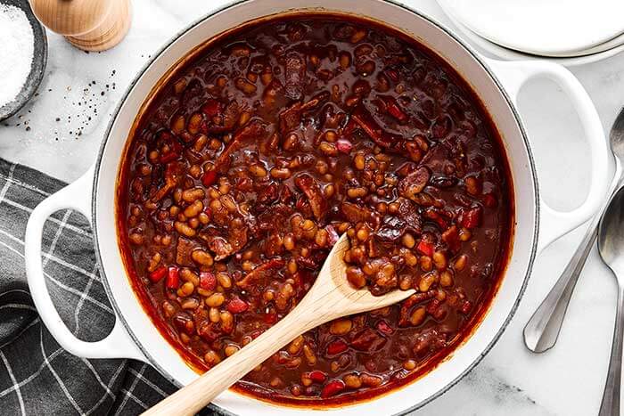 A white pot of baked beans with serving spoon.