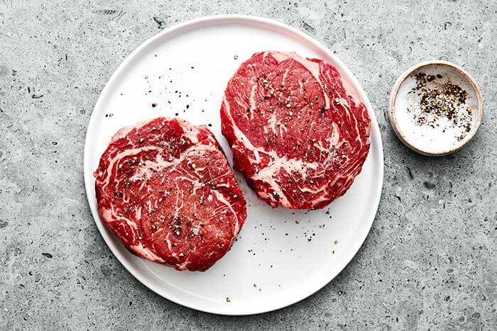 Raw ribeye steaks on a plate.