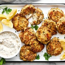Crab cakes on a platter with tartar sauce.