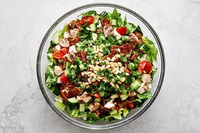 Mixing chicken bacon ranch chopped salad ingredients.