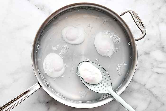 Making poached eggs in a stainless steel pan.