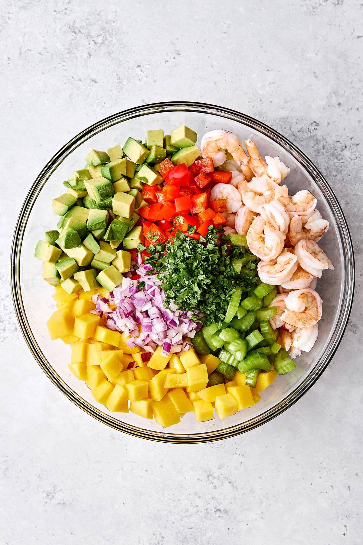 This mango avocado shrimp salad is sweet, crunchy, and tossed in a fresh honey lime dressing. It's the ultimate refreshing summer salad! Ingredients for mango avocado shrimp salad in a bowl.