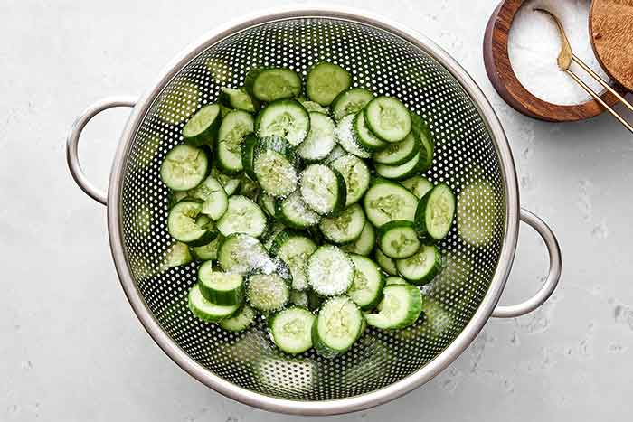 Salting cucumbers in colander.