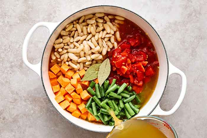 Adding broth to minestrone soup.