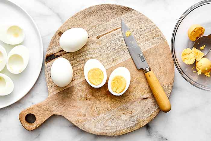 Slicing hard boiled eggs in half on a cutting board.
