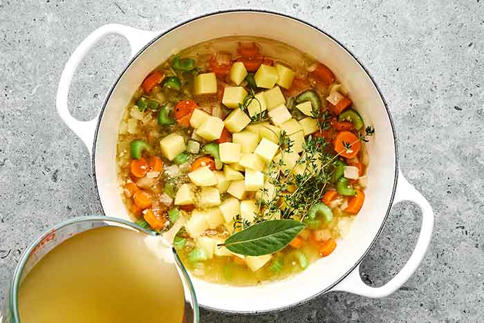 Adding potatoes and broth to turkey soup.