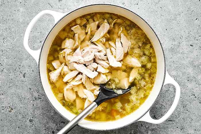 Adding shredded turkey to a pot of soup.