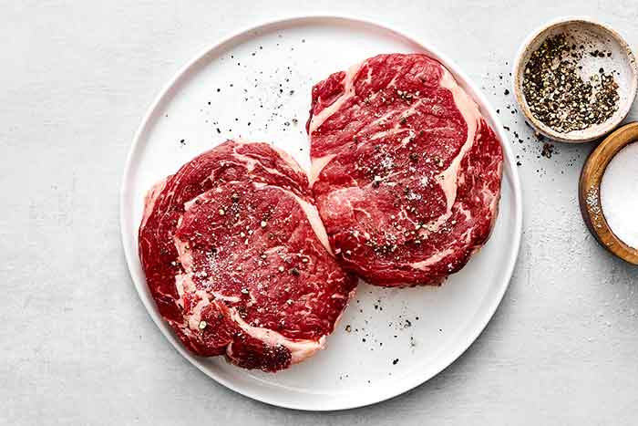 Step one: seasoning raw ribeye steaks.