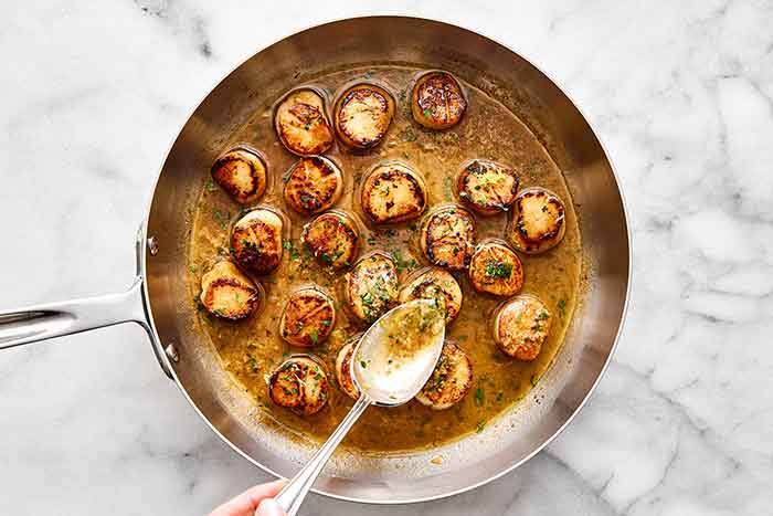 Step four of seared scallops: pour sauce over scallops.
