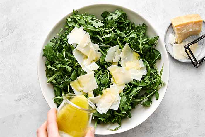 Adding lemon dressing to arugula salad.