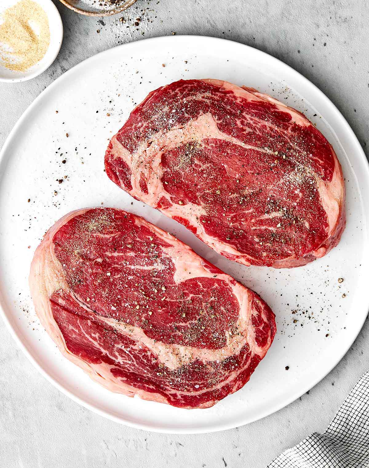 Seasoning ribeye steaks on a plate.