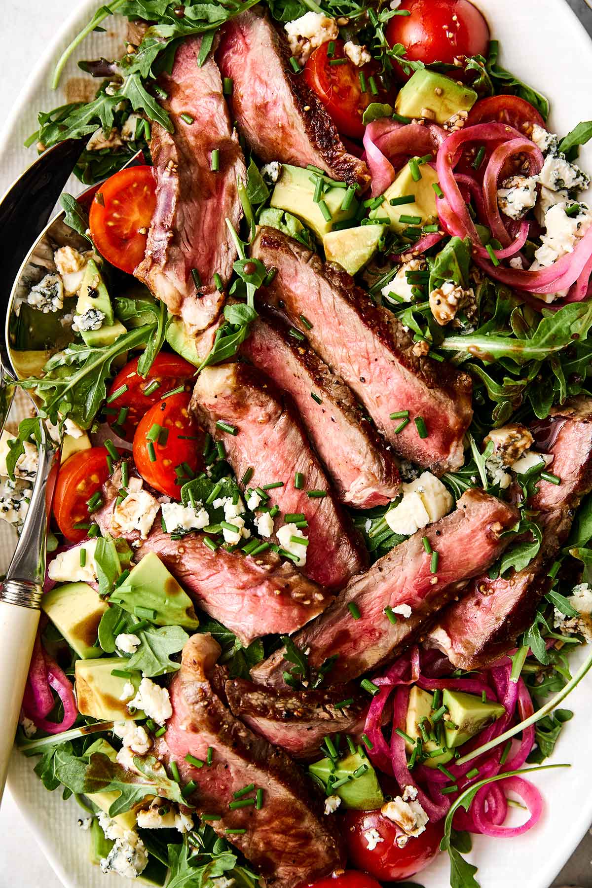This steak salad piled high with grilled steak, arugula, fresh veggies, and a balsamic dressing is my favorite summer salad yet! Summer steak salad with blue cheese.